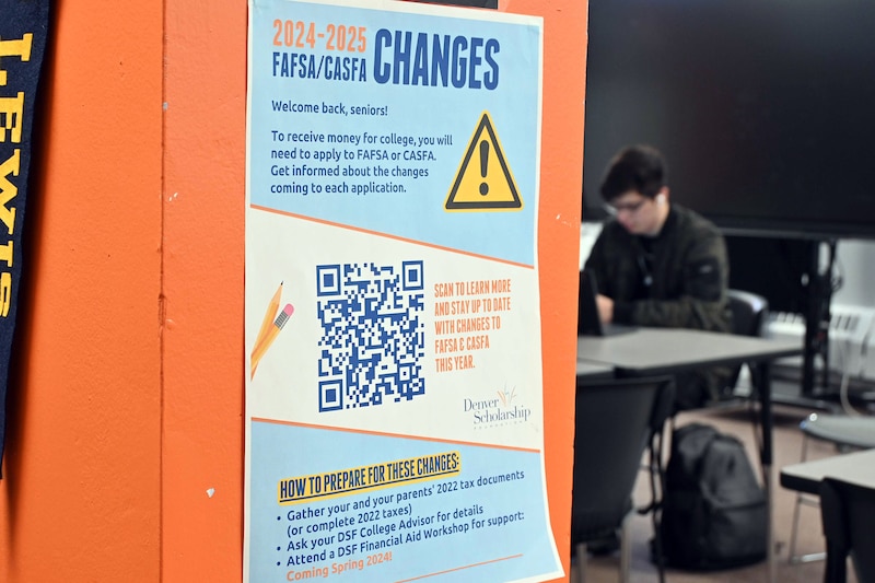 A colorful poster is seen attached to a wall in the foreground with an out of focus high school student sitting at a desk in the background.