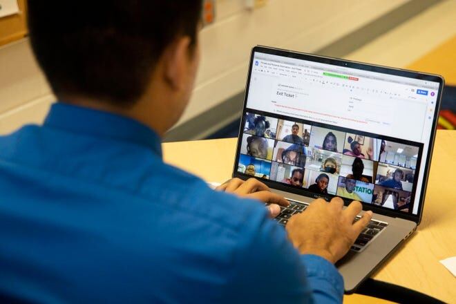 A teacher faces his laptop where students are shown on the screen for an online class.