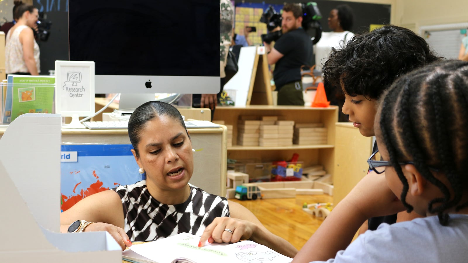 A woman points at a page in a book while two students watch