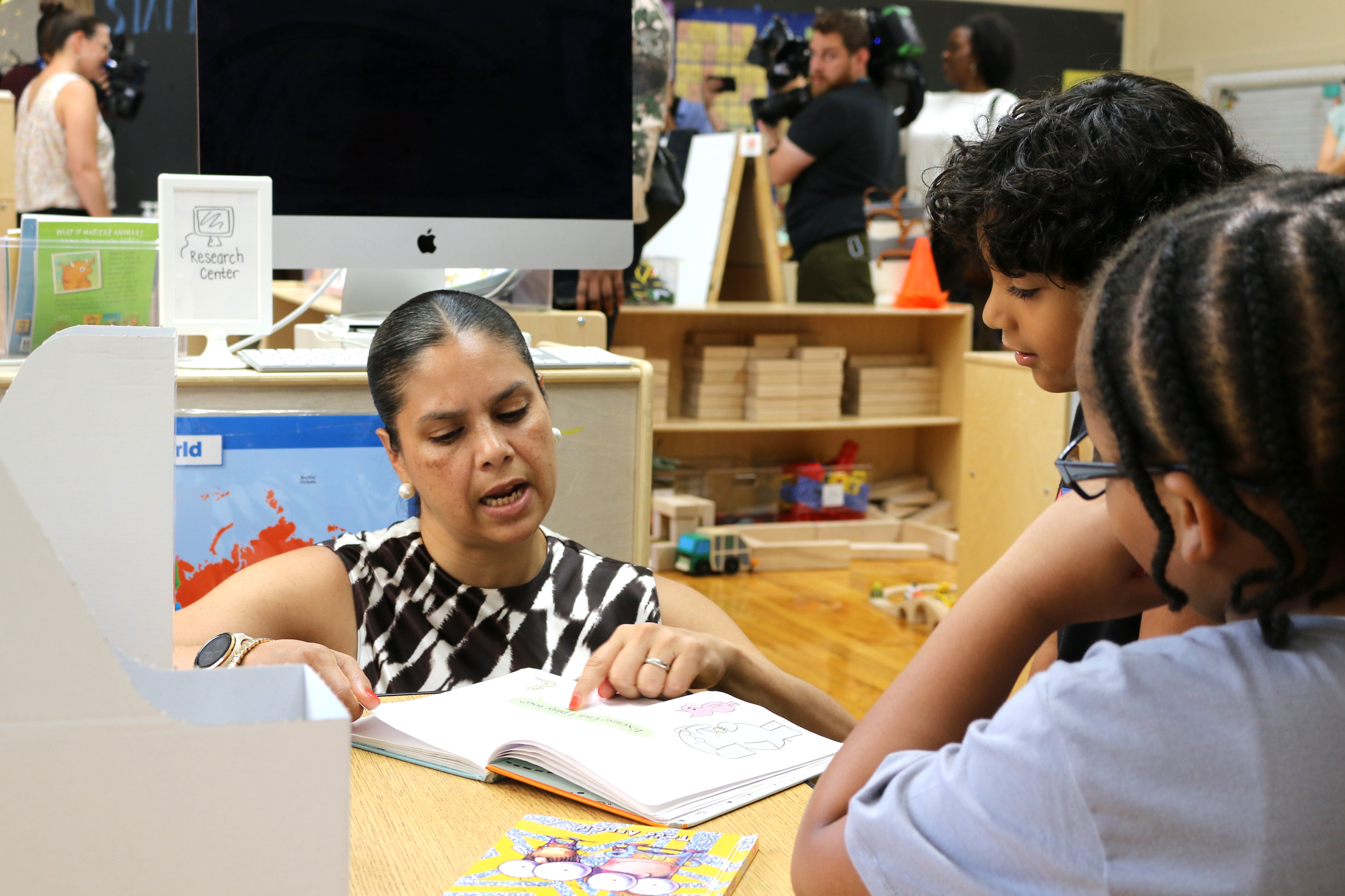 A woman points at a page in a book while two students watch