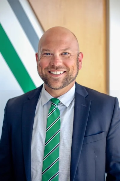 Headshot of a man with a beard. He wears a dark blazer, a light shirt, and a green tie.