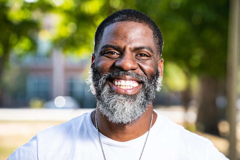 A man wearing a white t-shirt poses for a portrait outside.