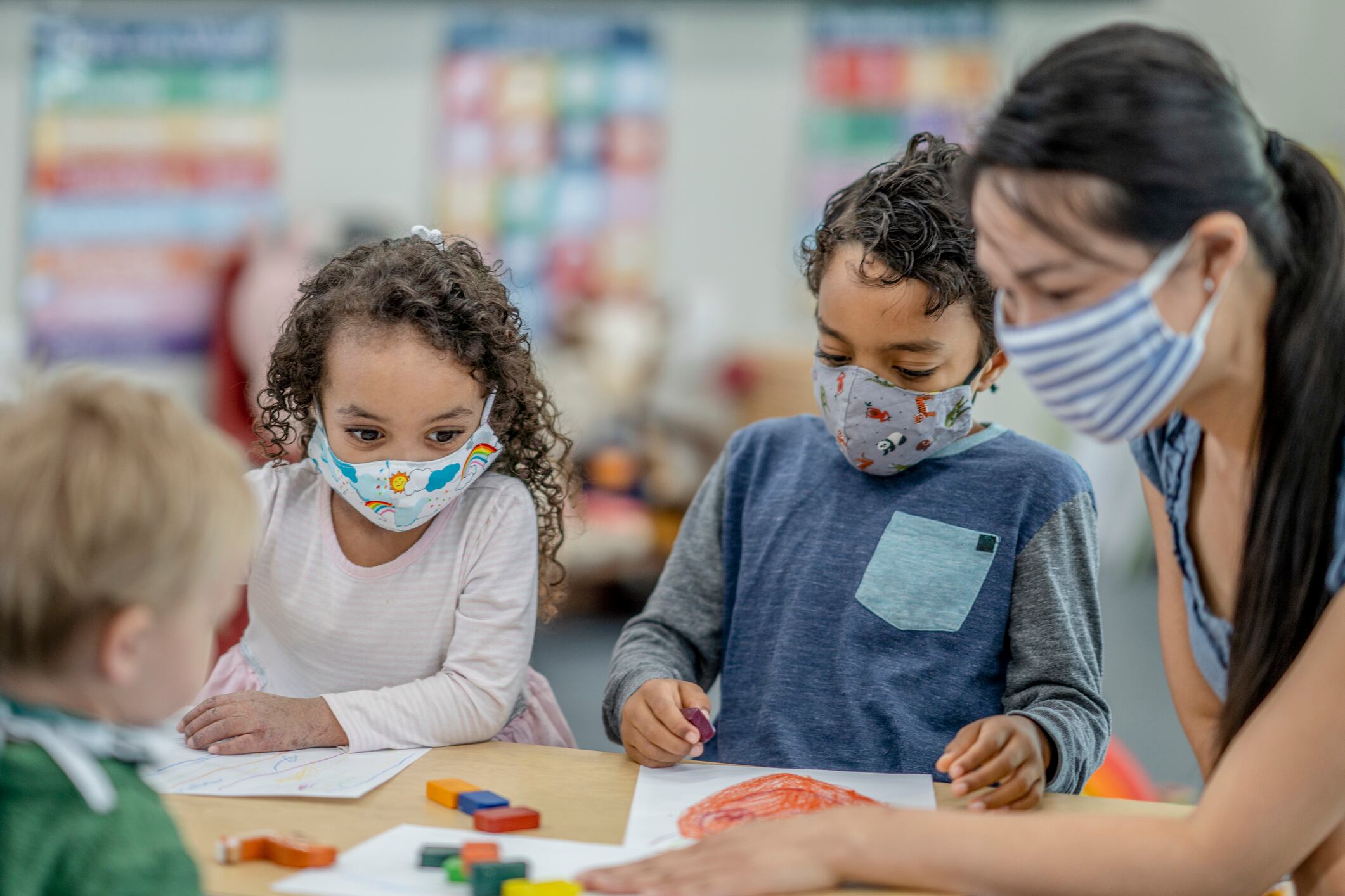 Children coloring at a table while wearing protective face masks.