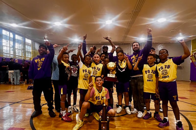 A photograph of a young school basketball team posing with a trophy in a school gym.