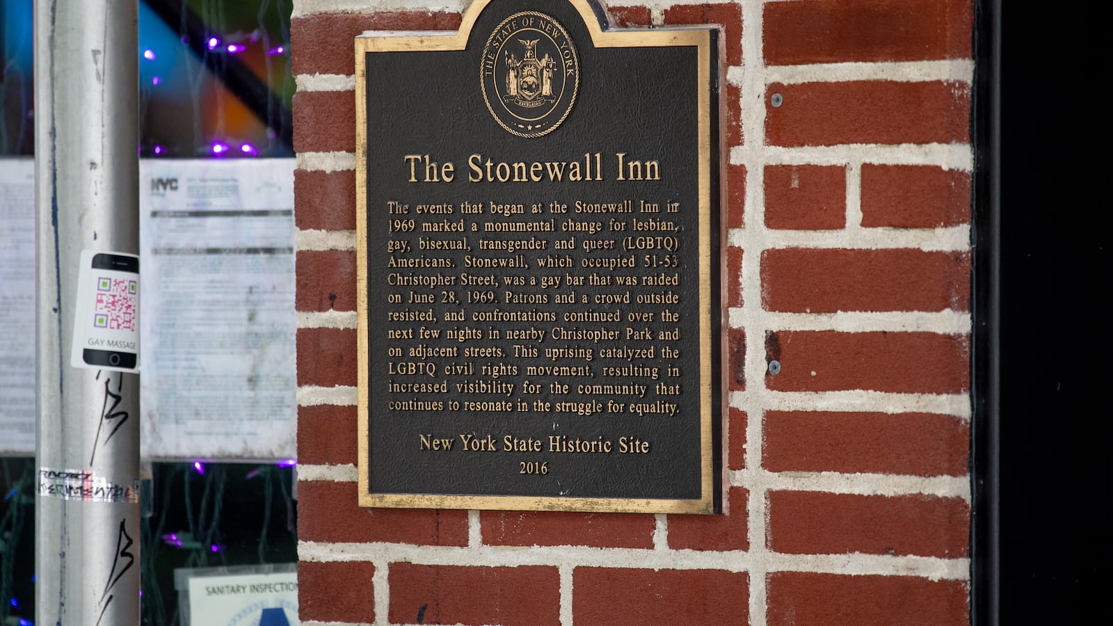 A black and gold sign on a brick wall denotes the Stonewall Inn in New York City as a New York State Historic Site.