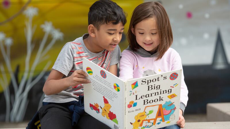 A young girl and boy sit together reading a book called “Spot’s Big Learning Book.”