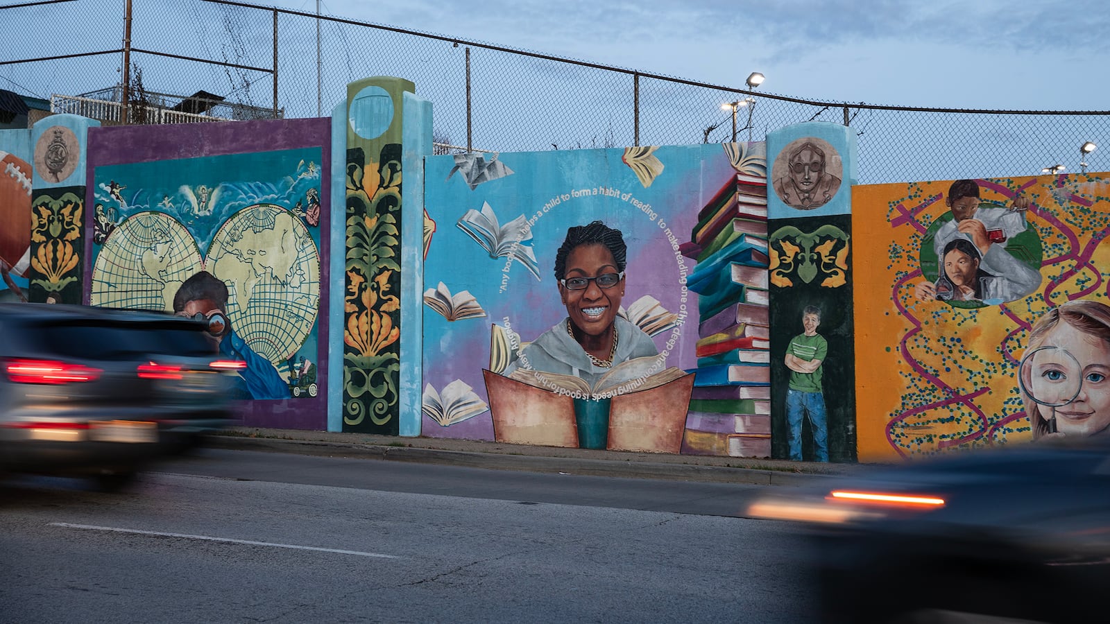 Cars blur by a colorful mural with students and guardians with a dark blue sky in the background.