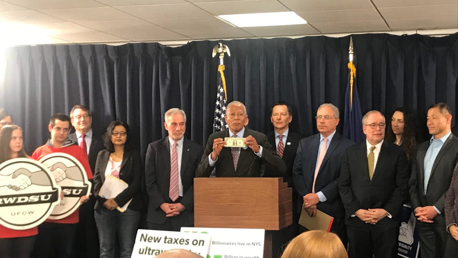 Manhattan Sen. Robert Jackson holds up a dollar bill as he and others advocate for a wealth tax to help fill the state's expected budget shortfall.