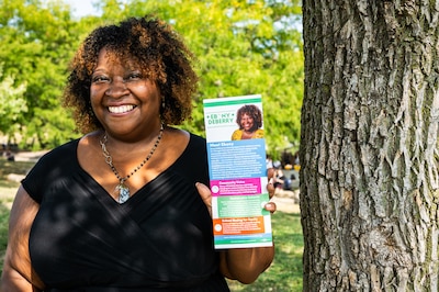 A woman in a dark top holds a pamphlet.