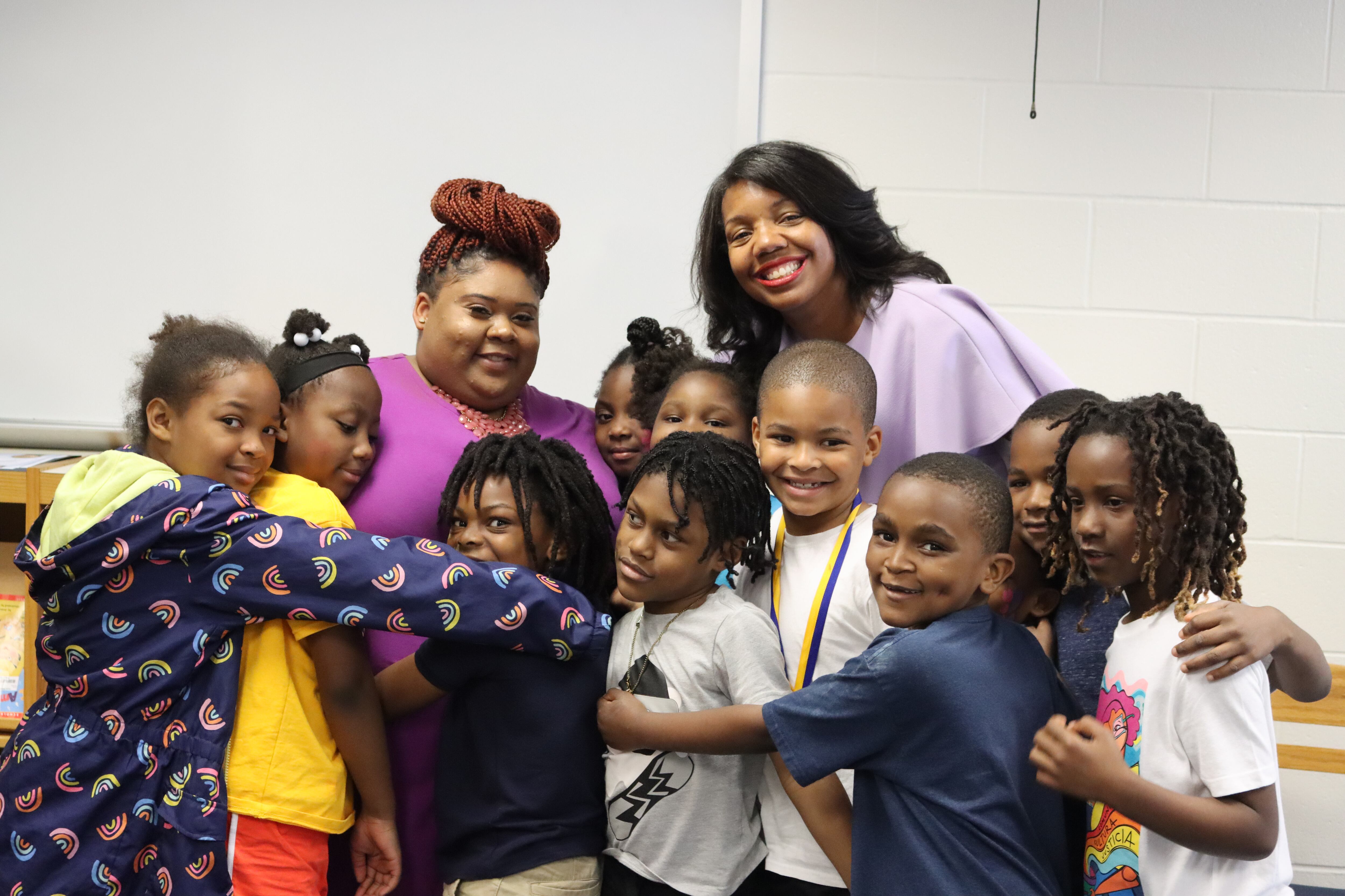 Two women stand behind a group of students in a group hug.