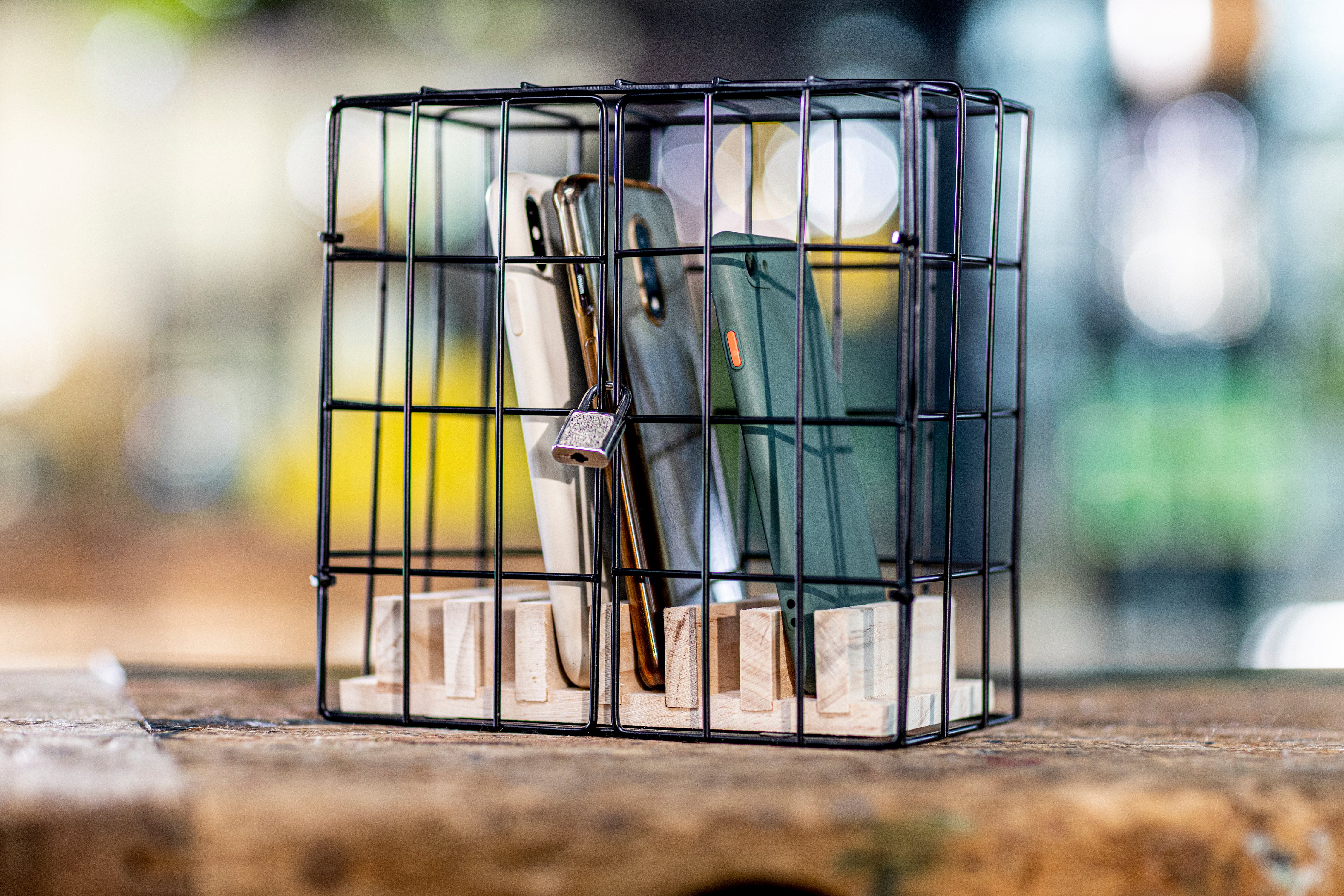 Three cell phones on a wood surface locked in a cage.