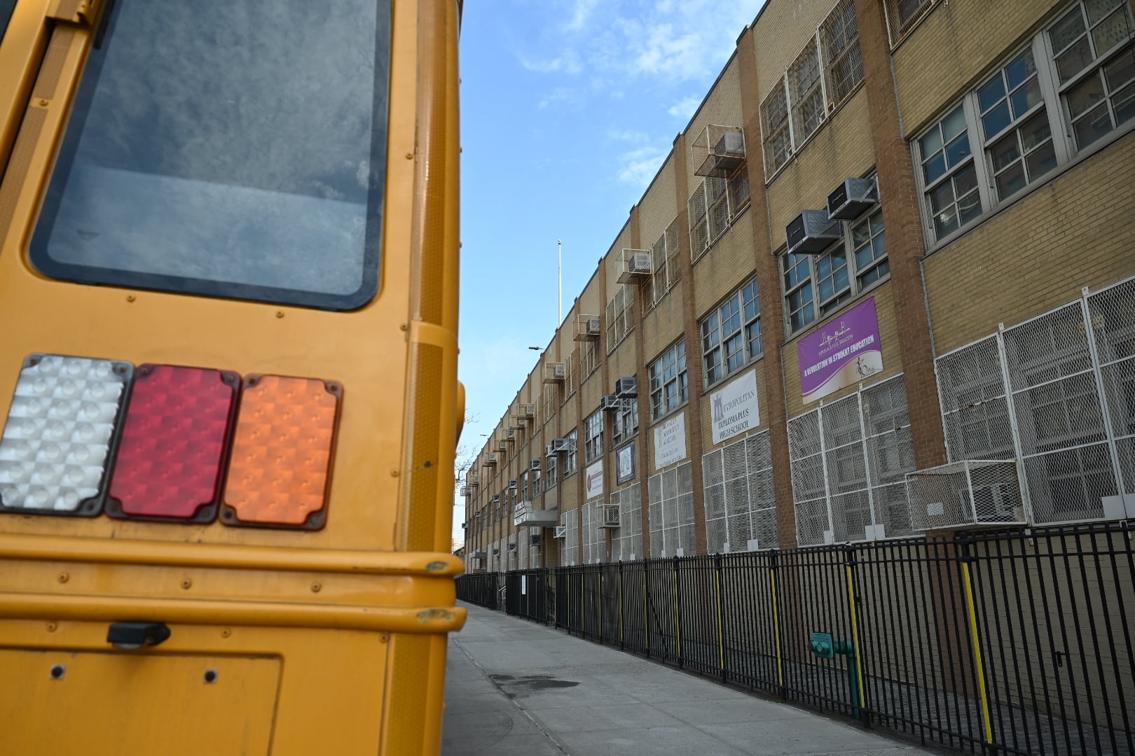 A close up of the back of a yellow school bus next to a school building.