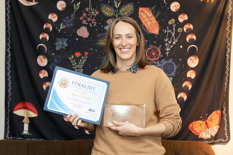 A woman in a tan sweater holds an object and a document.