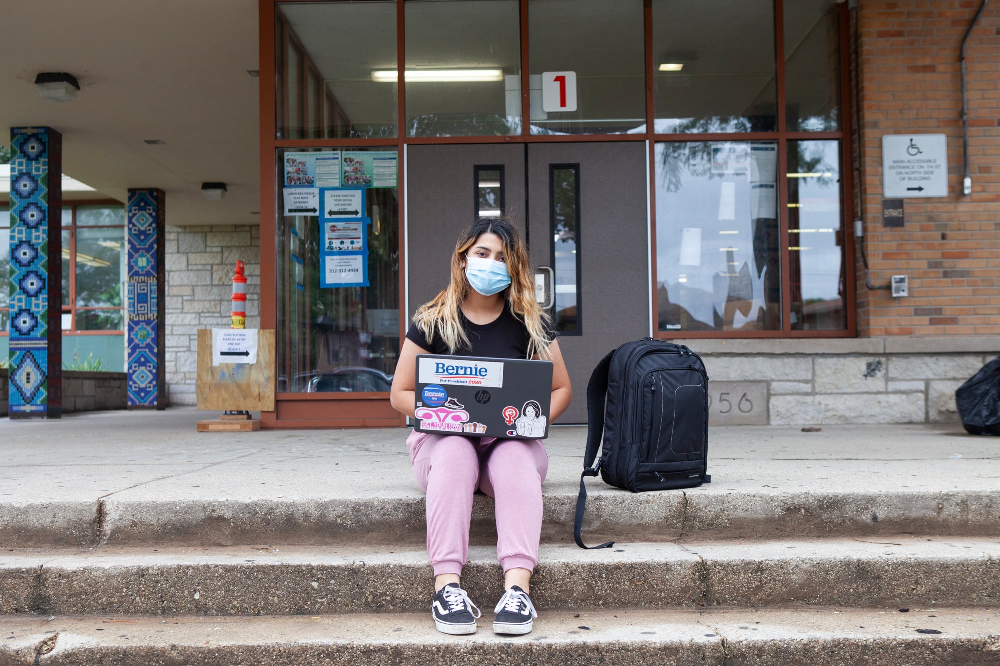 Trinity sitting on the steps outside of school with her backpack and laptop.
