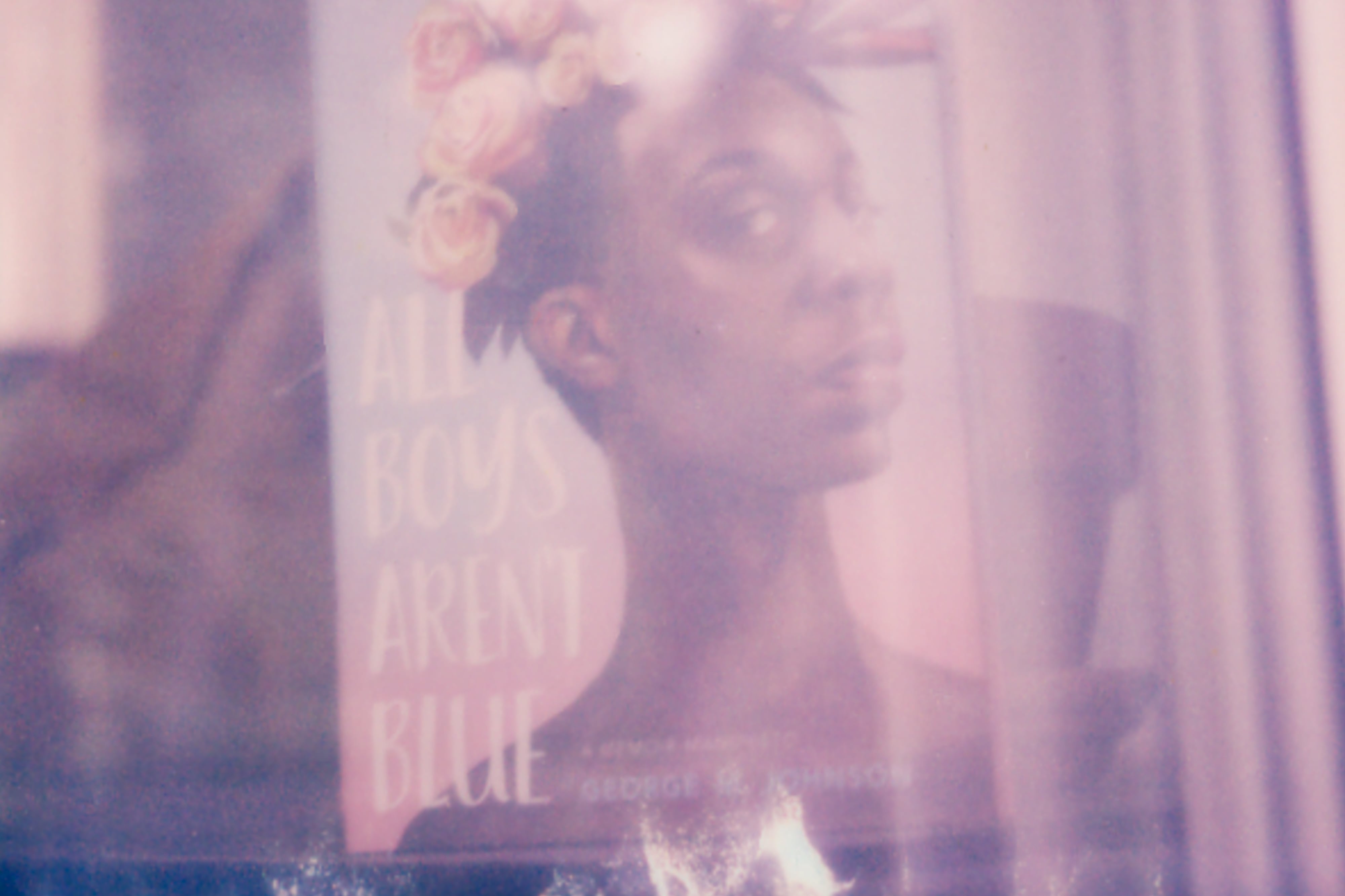 The book “All Boys Aren’t Blue” by George M. Johnson sits in a windowsill, the cover showing a Black man posing with a bouquet of flowers on his head.