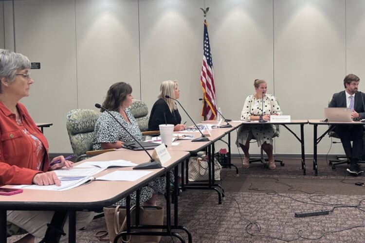 Five people sit around a conference table with an American flag in the background.