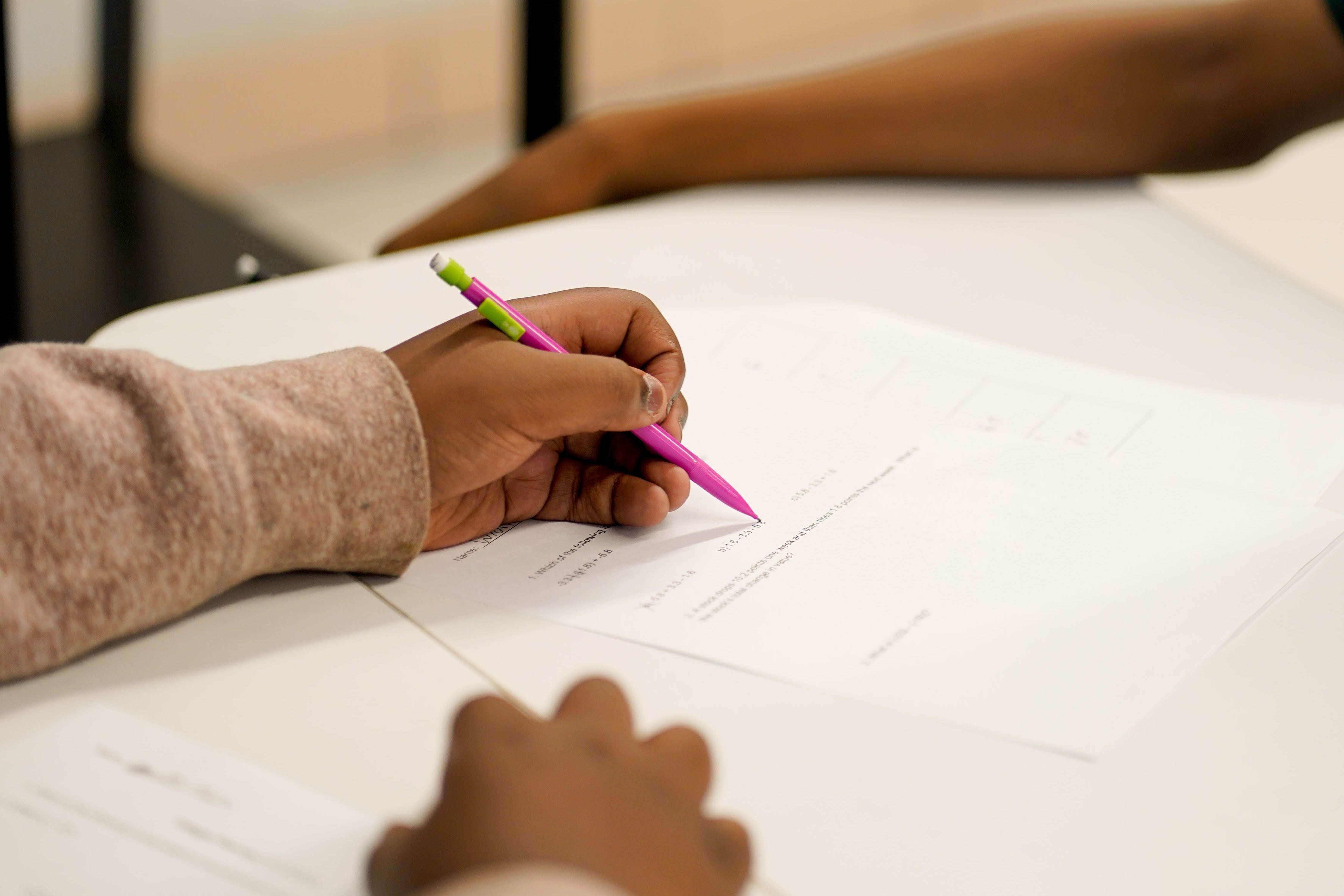 A close up of a Black students' hands filling out a worksheet.