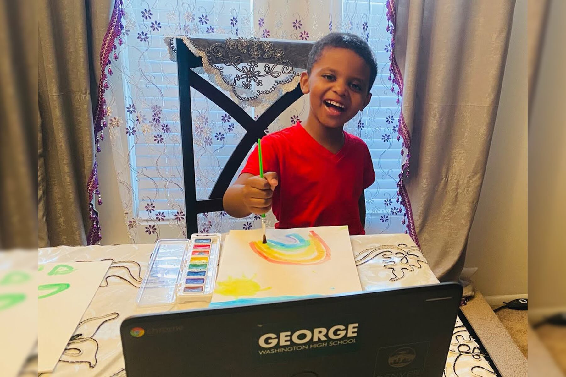 Moumin Elgizoli in front of a laptop painting a rainbow picture.