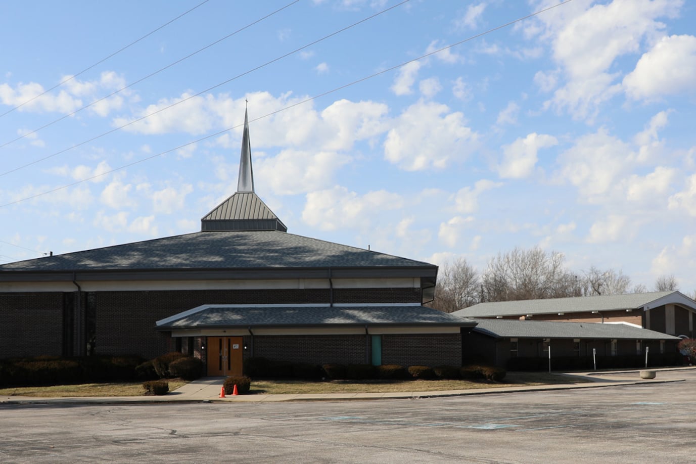 A building with a large top and a parking lot in the foreground and a blue sky with clouds in the background.