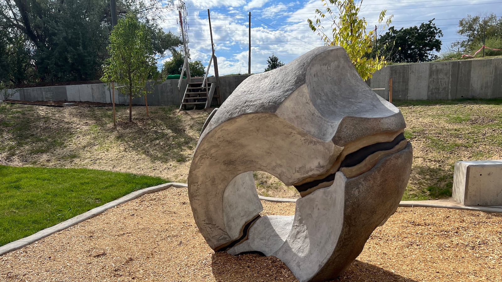A large, round rock on sits outside on top of wood chips with a fence in the background.