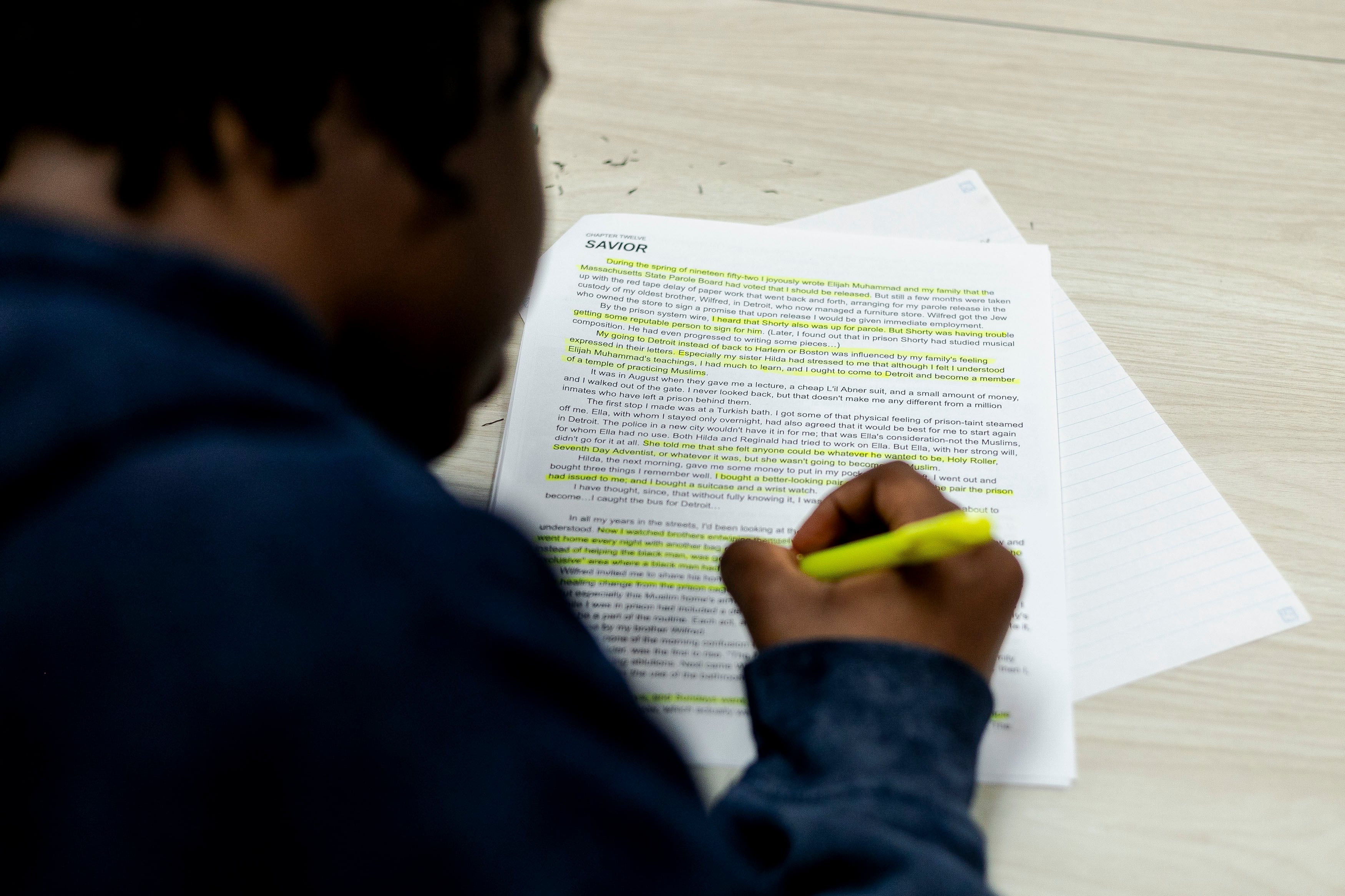 A high school student highlights text on a sheet of paper on a desk.