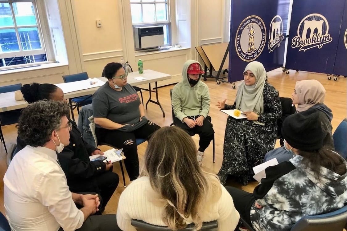 A group of people sit in a circle in a room having a conversation.