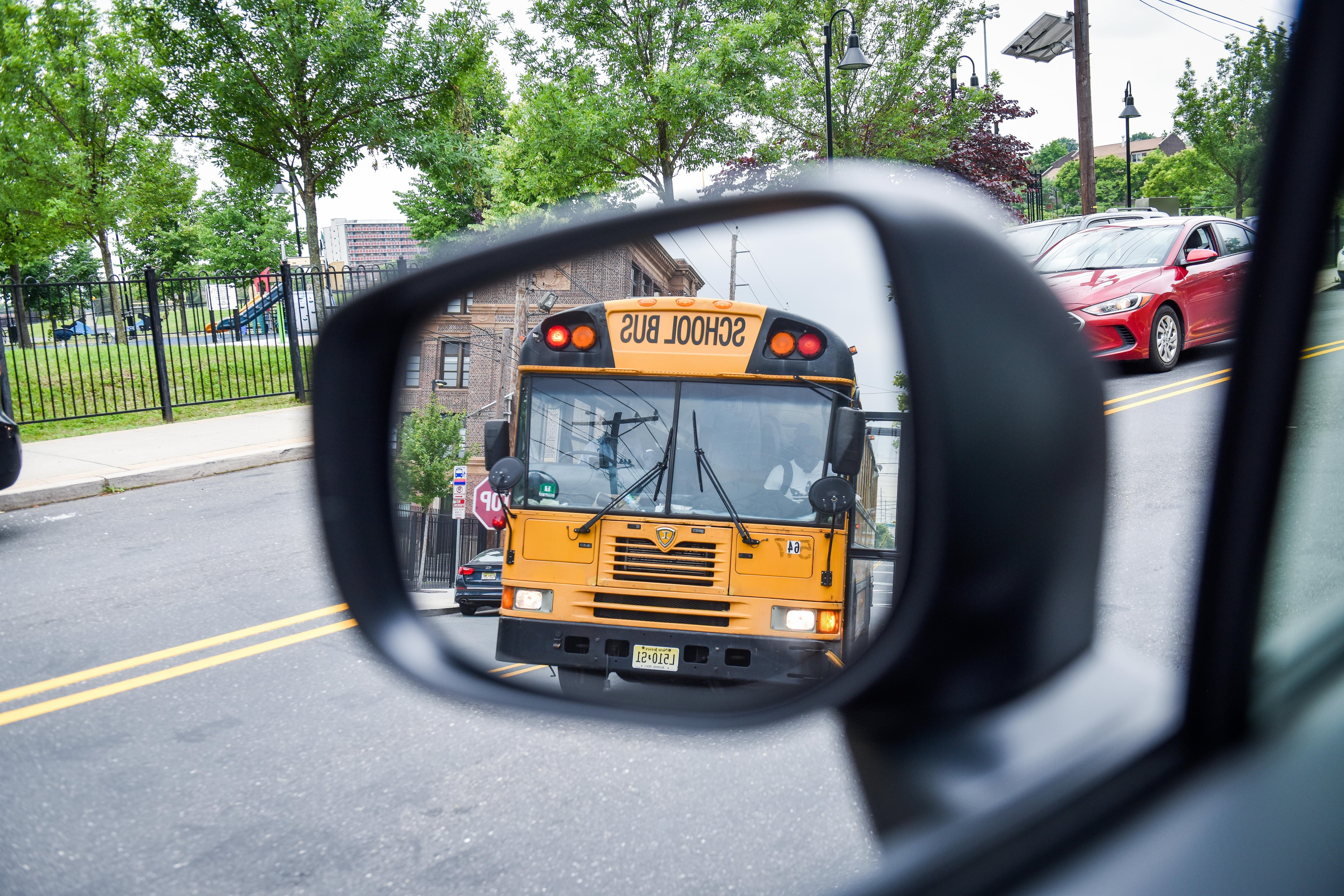 A yellow school bus is seen in the reflection of a car's sideview mirror.