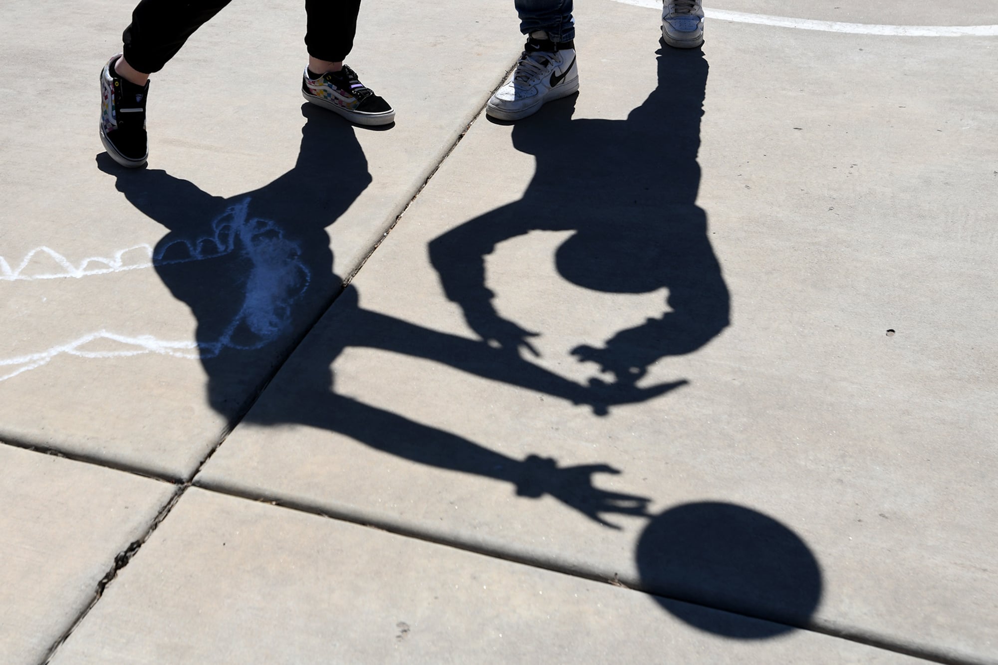 The shadows of children playing can be seen on the blacktop.