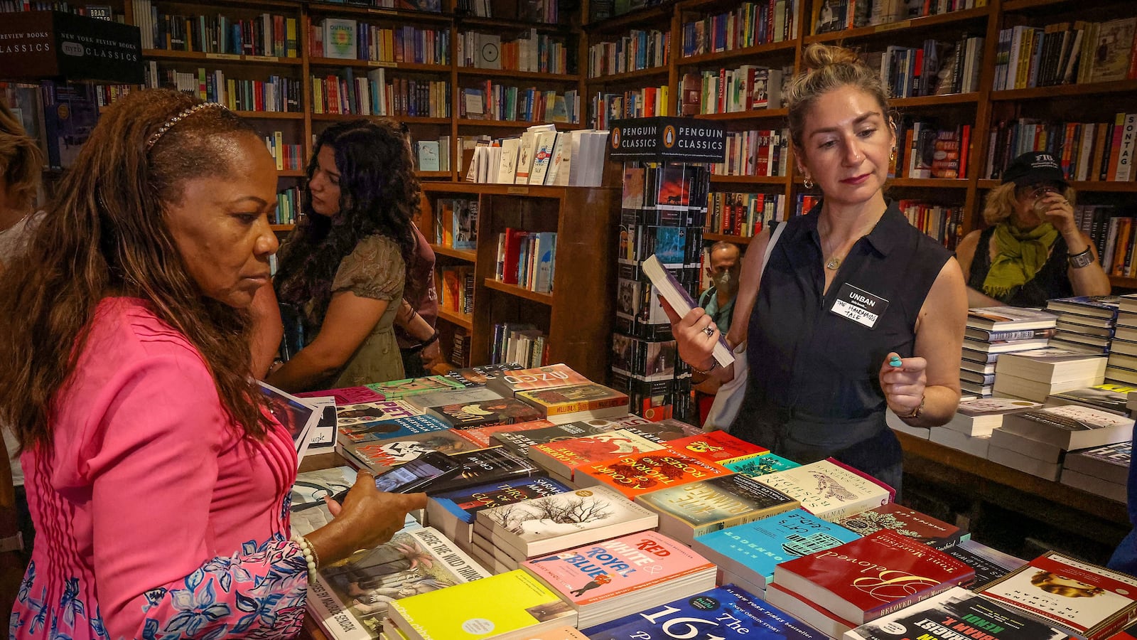 Two women stand on either side of a table filled with books.