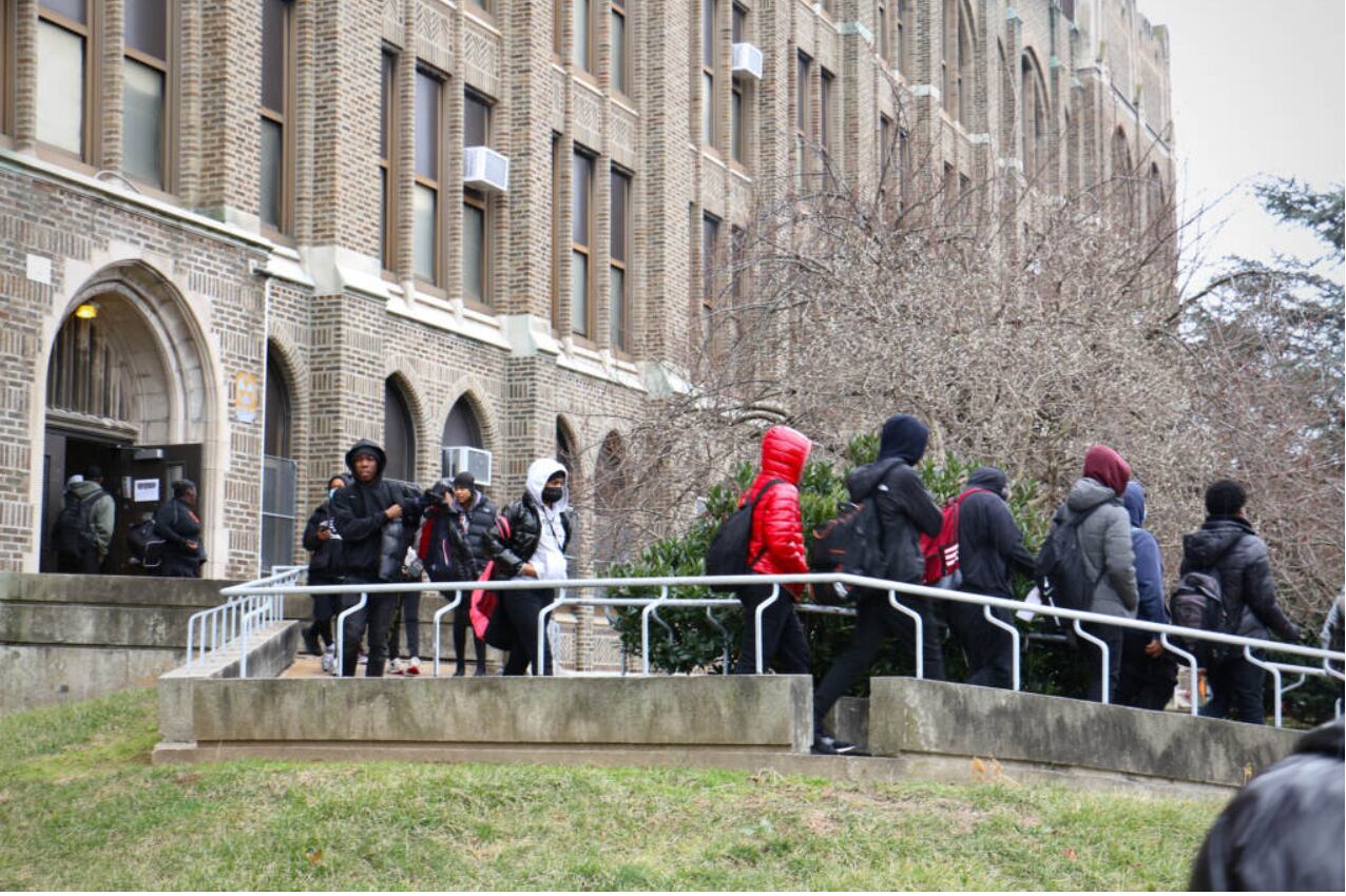 Several children wearing jackets and other cold-weather clothing leave a brick and stone building.