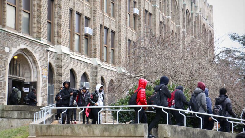 Several children wearing jackets and other cold-weather clothing leave a brick and stone building.