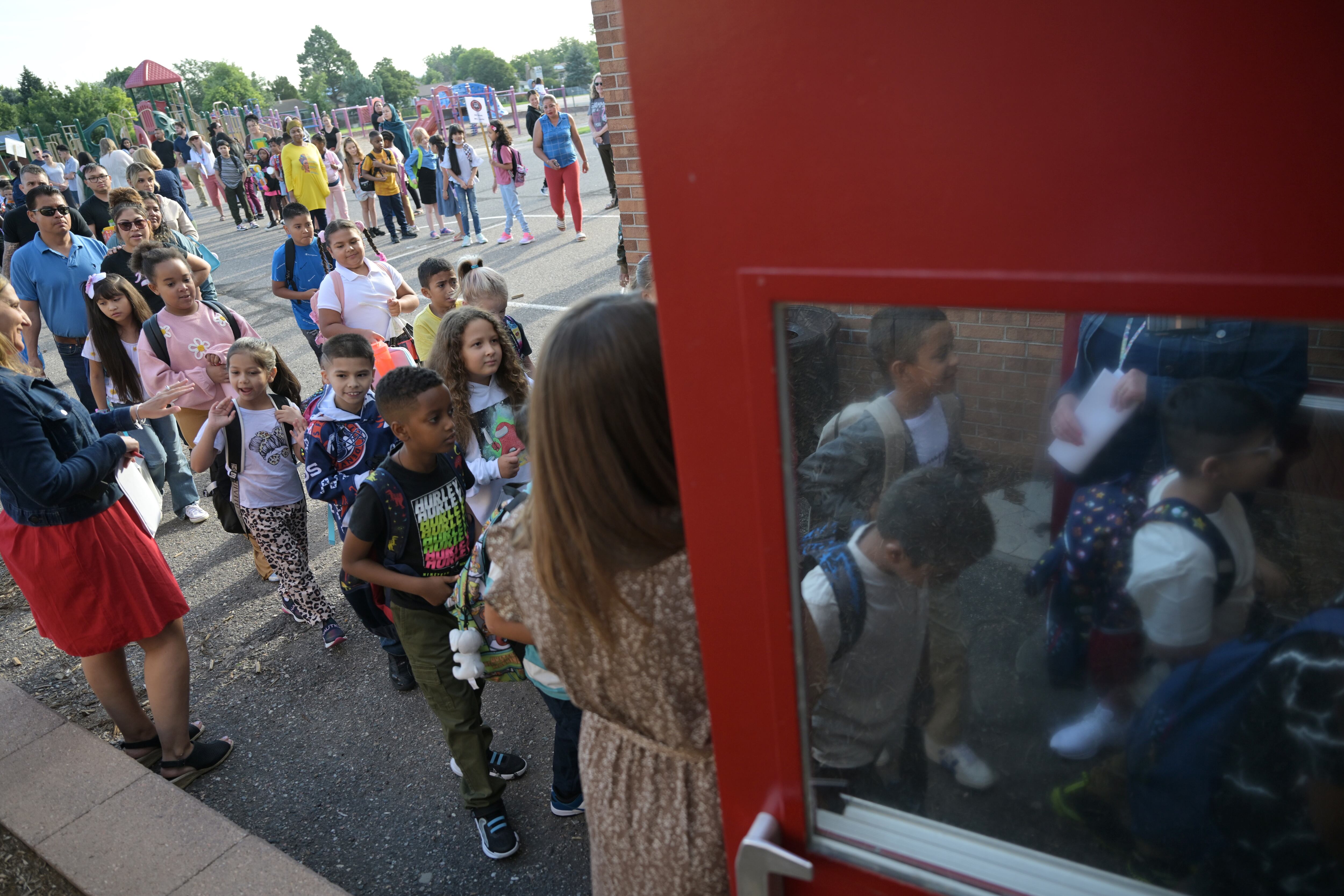 Young children in backpacks and new outfits walk off the playground and through a large red door.