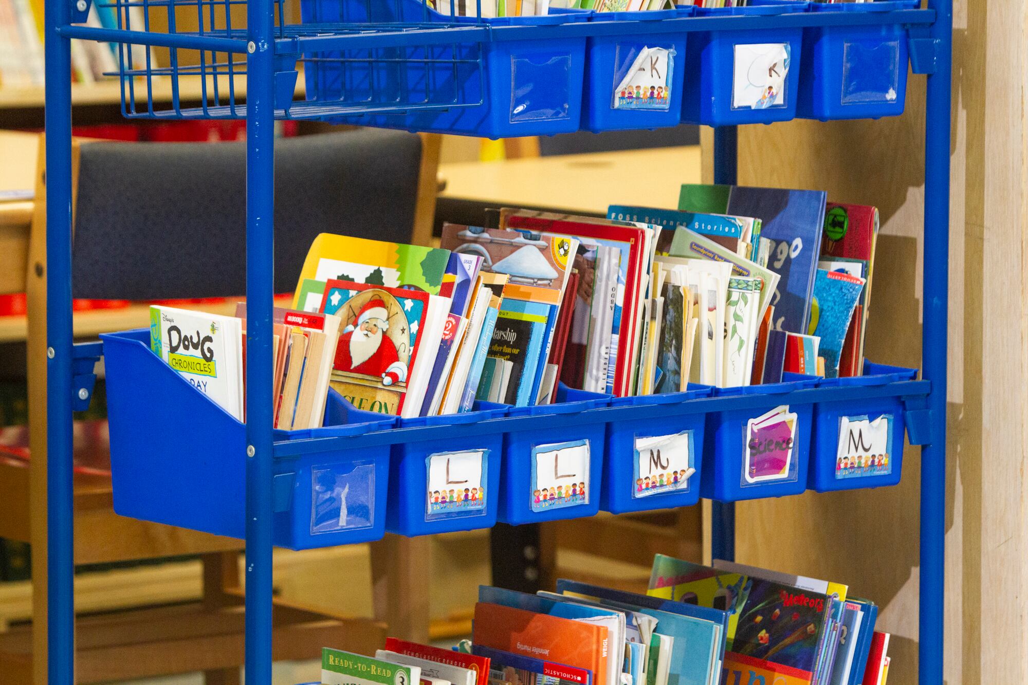 A blue cart of picture books organized alphabetically.