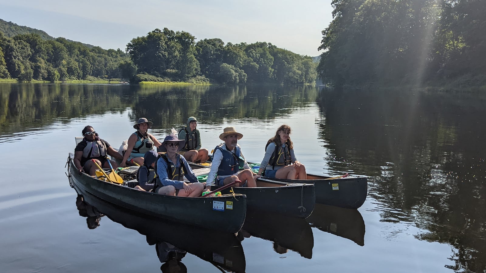 A group of teachers wearing lifejackets sit in three canoes