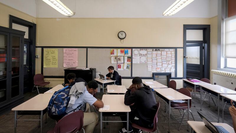 Four or five male students sit looking down in a classroom