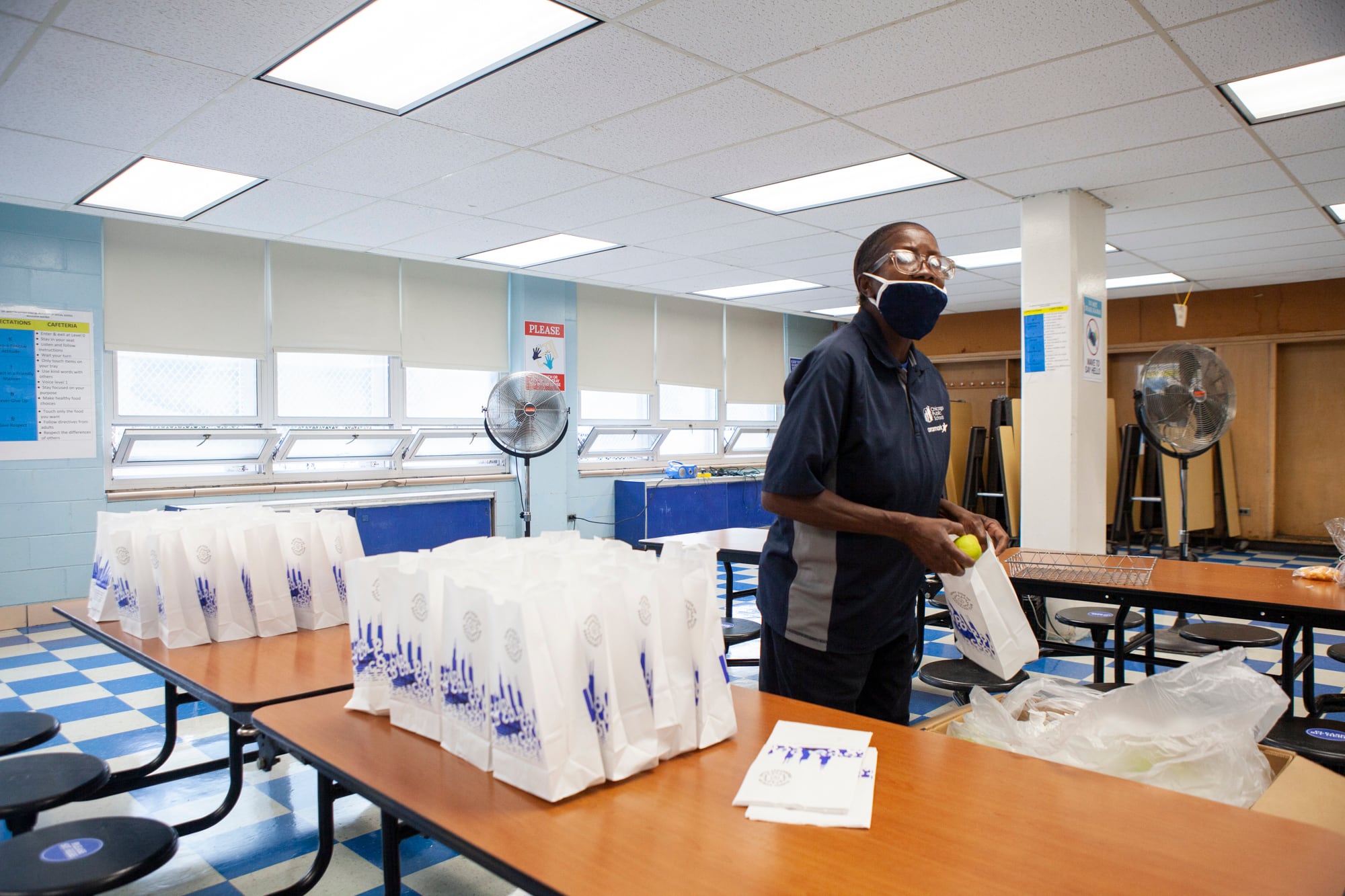 A food service worker wearing a face mask assembles white lunch bags.