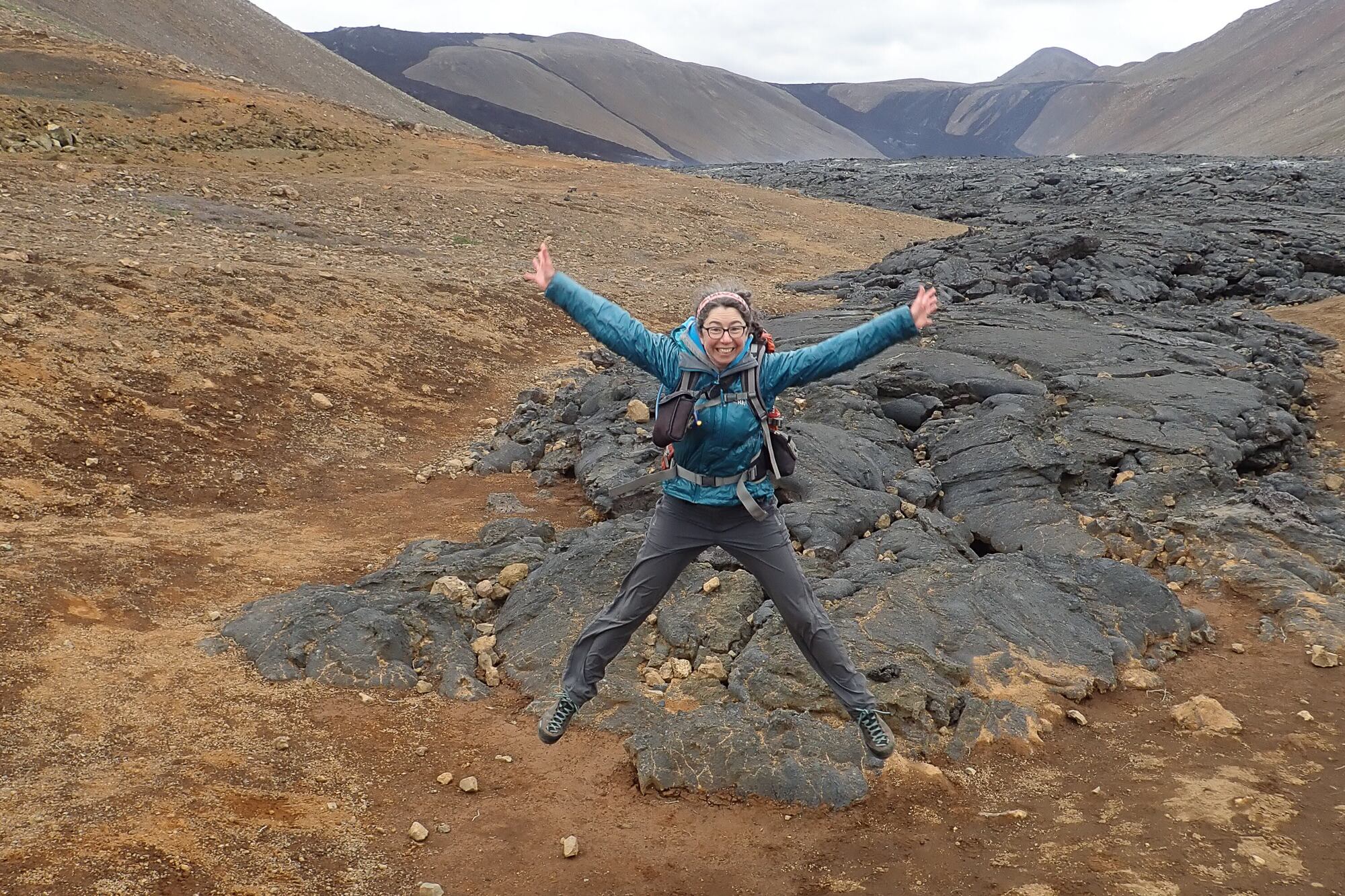A woman jumping off the ground with her arms and legs outstretched in a volcanic area in Iceland.
