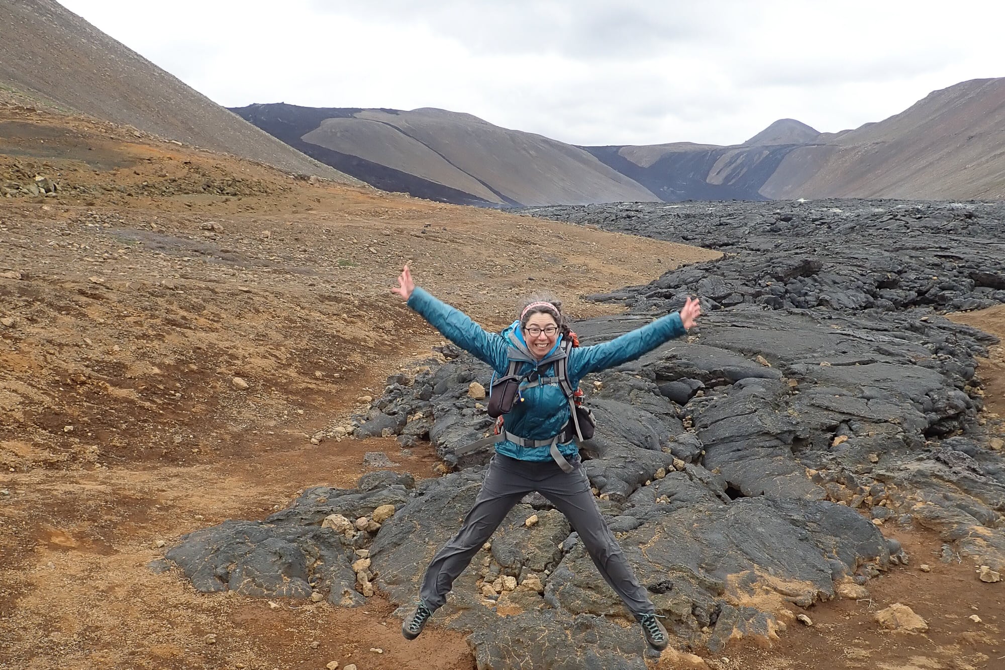 A woman jumping off the ground with her arms and legs outstretched in a volcanic area in Iceland.
