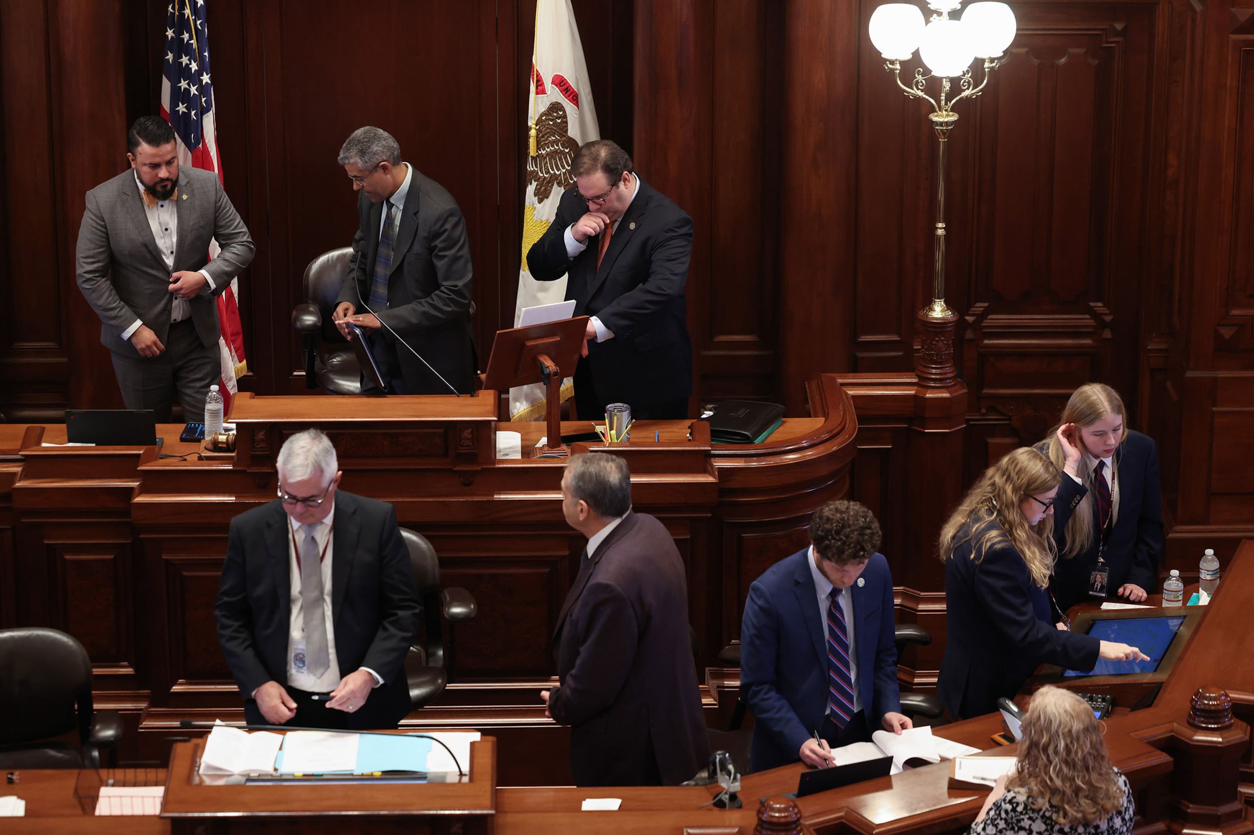 A photograph of a group of people in suits at a two level podium in the Illinois state Capitol building.