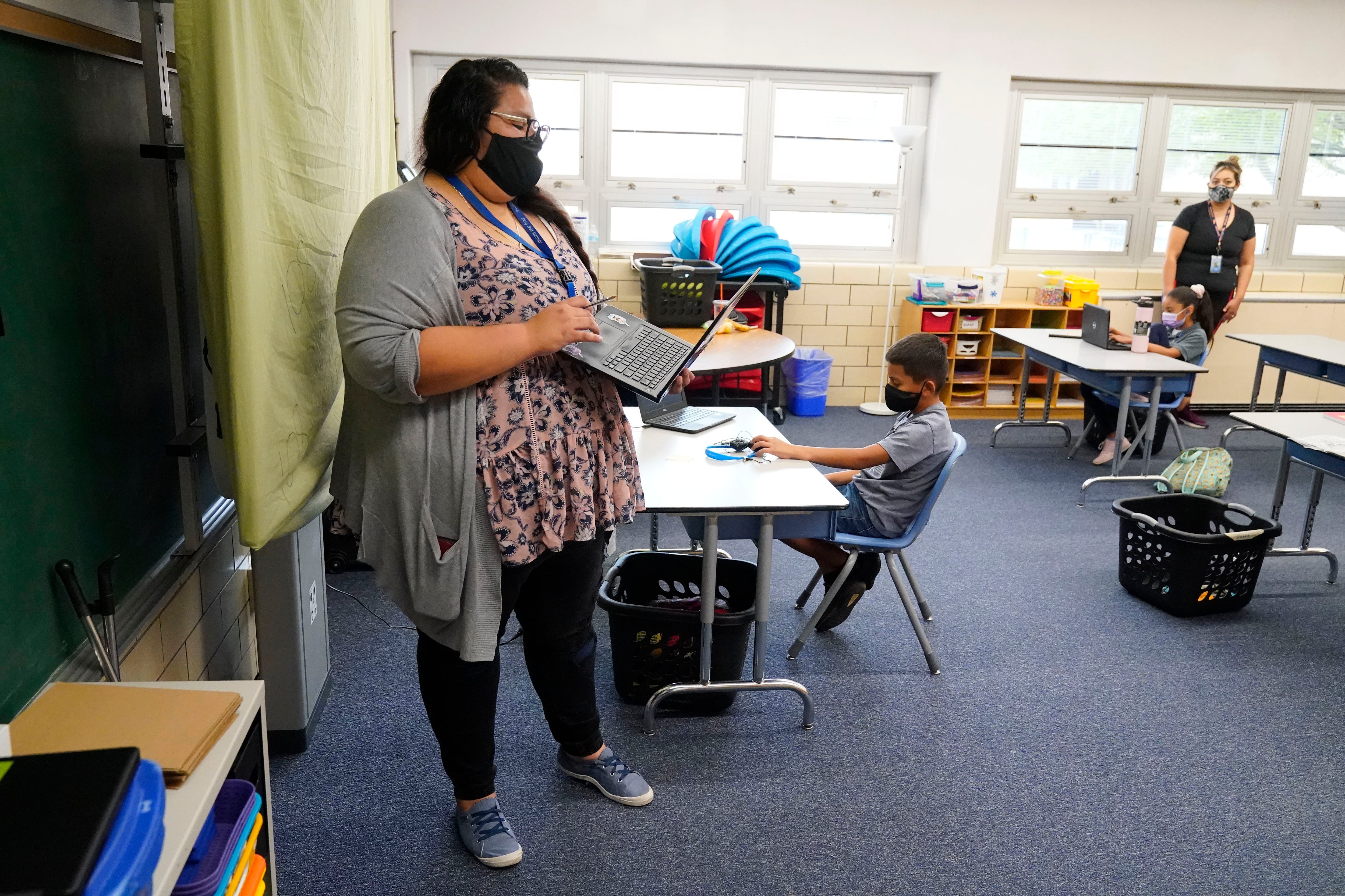 Teacher wearing a mask supervises students at a learning center.