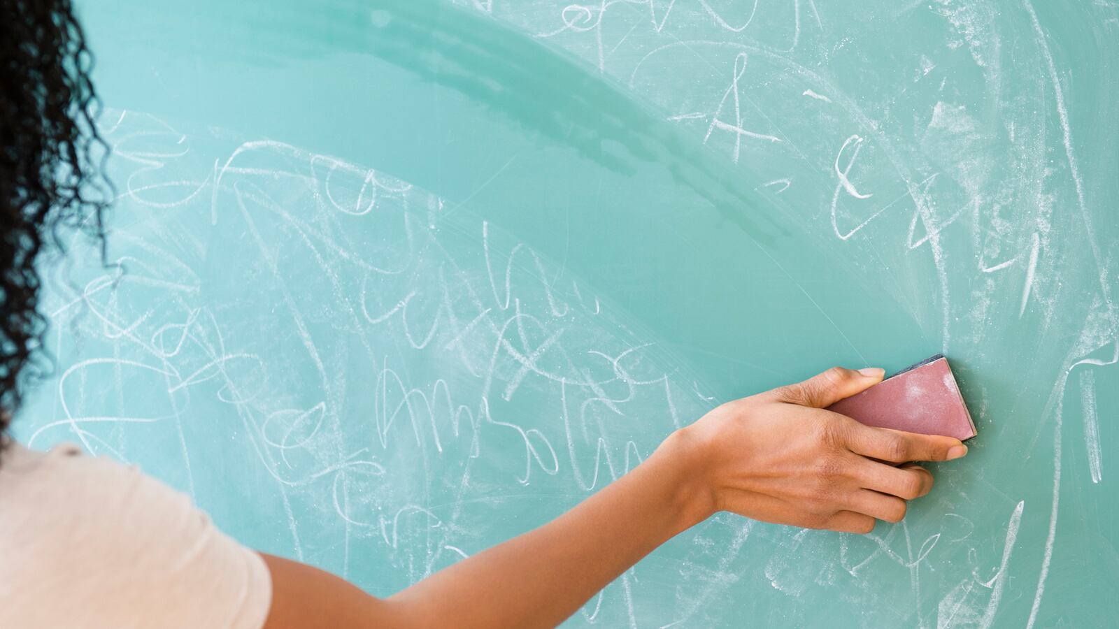 A teacher erases writing on a chalkboard.