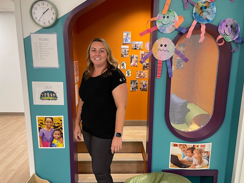 A woman in a black shirt stands in front of a colorful nook in a preschool classroom.
