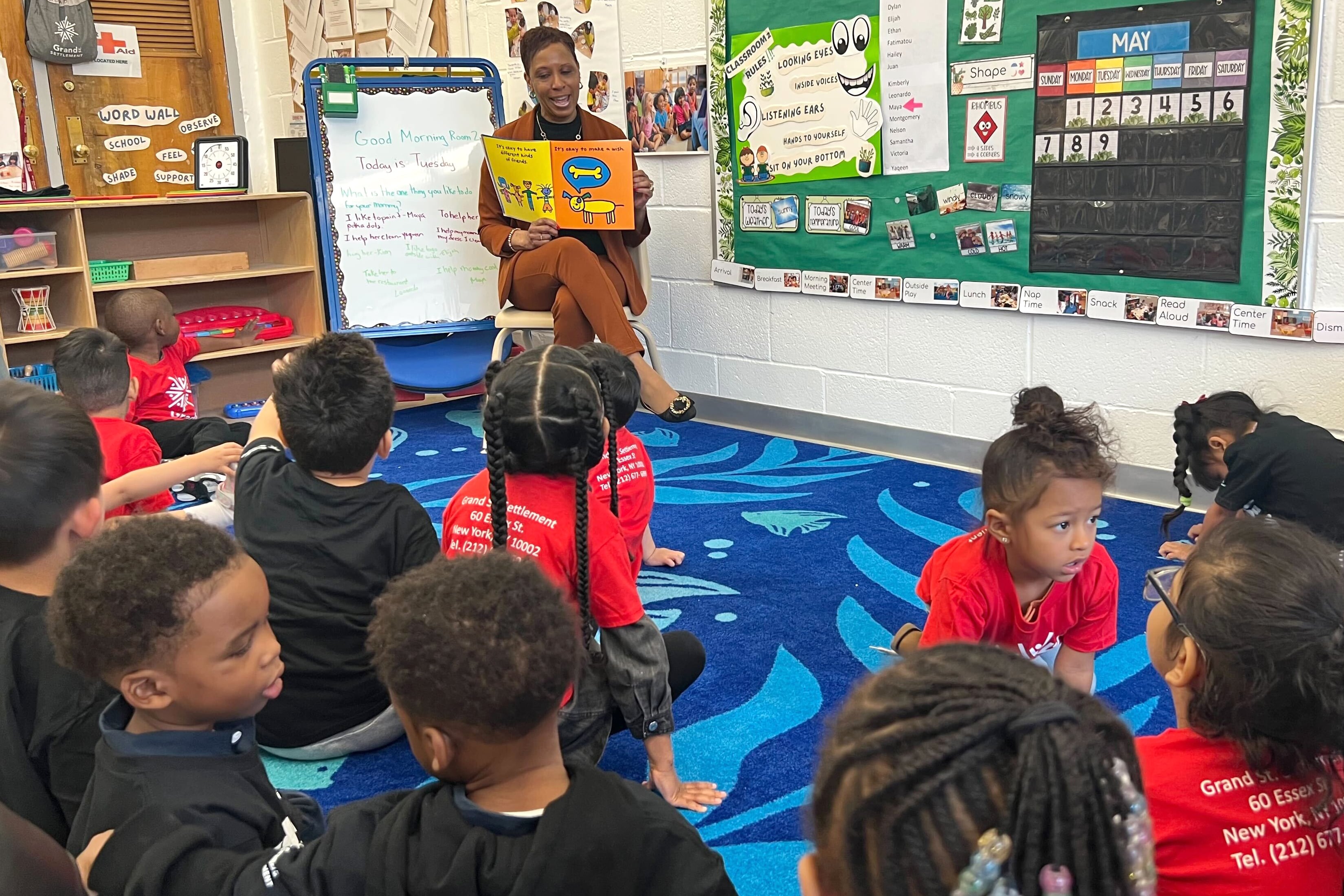 woman in orange pantsuit reads to students