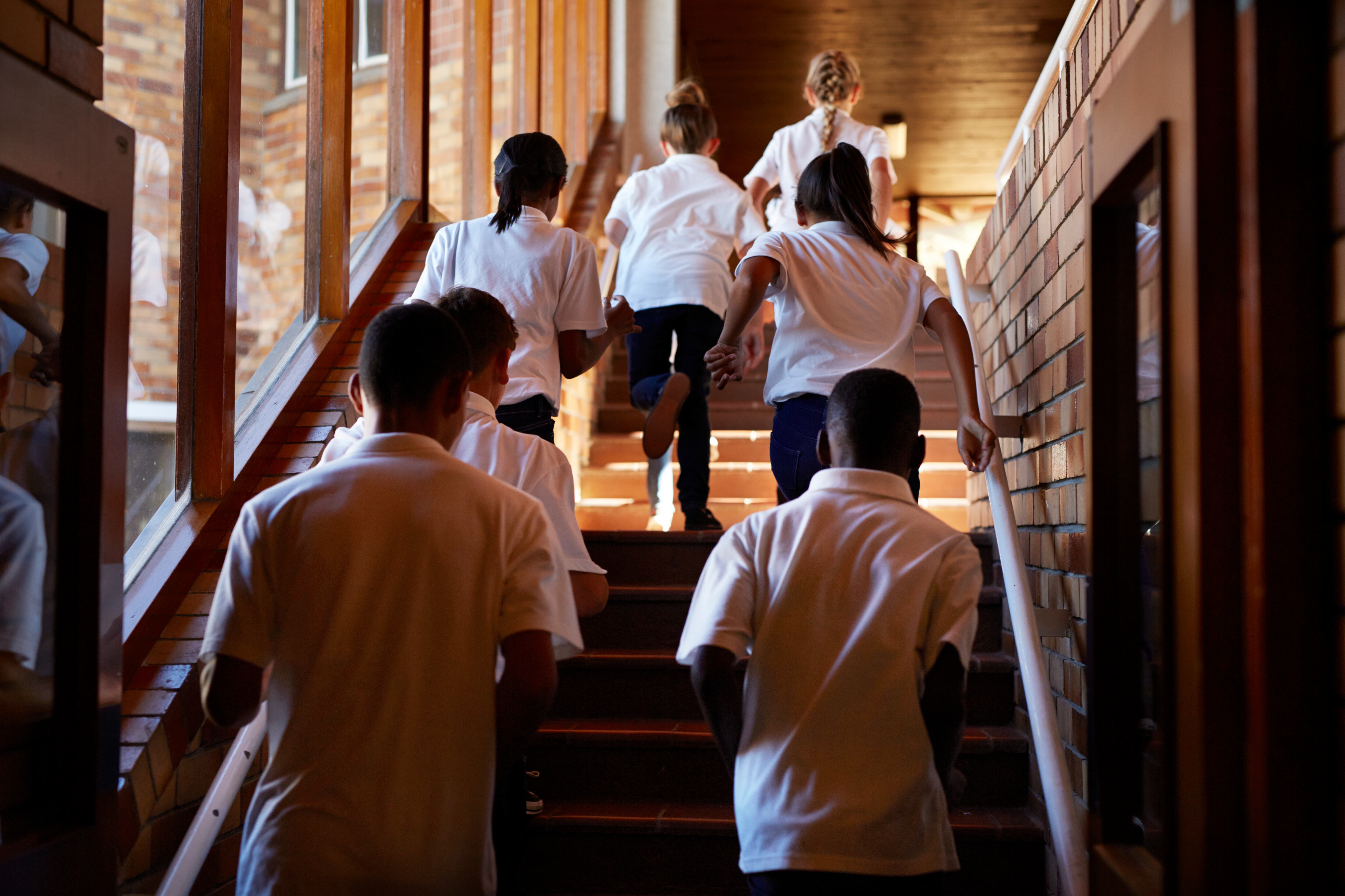 A group of seven students wearing white shirts as part of a uniform run up the stairs in a school.