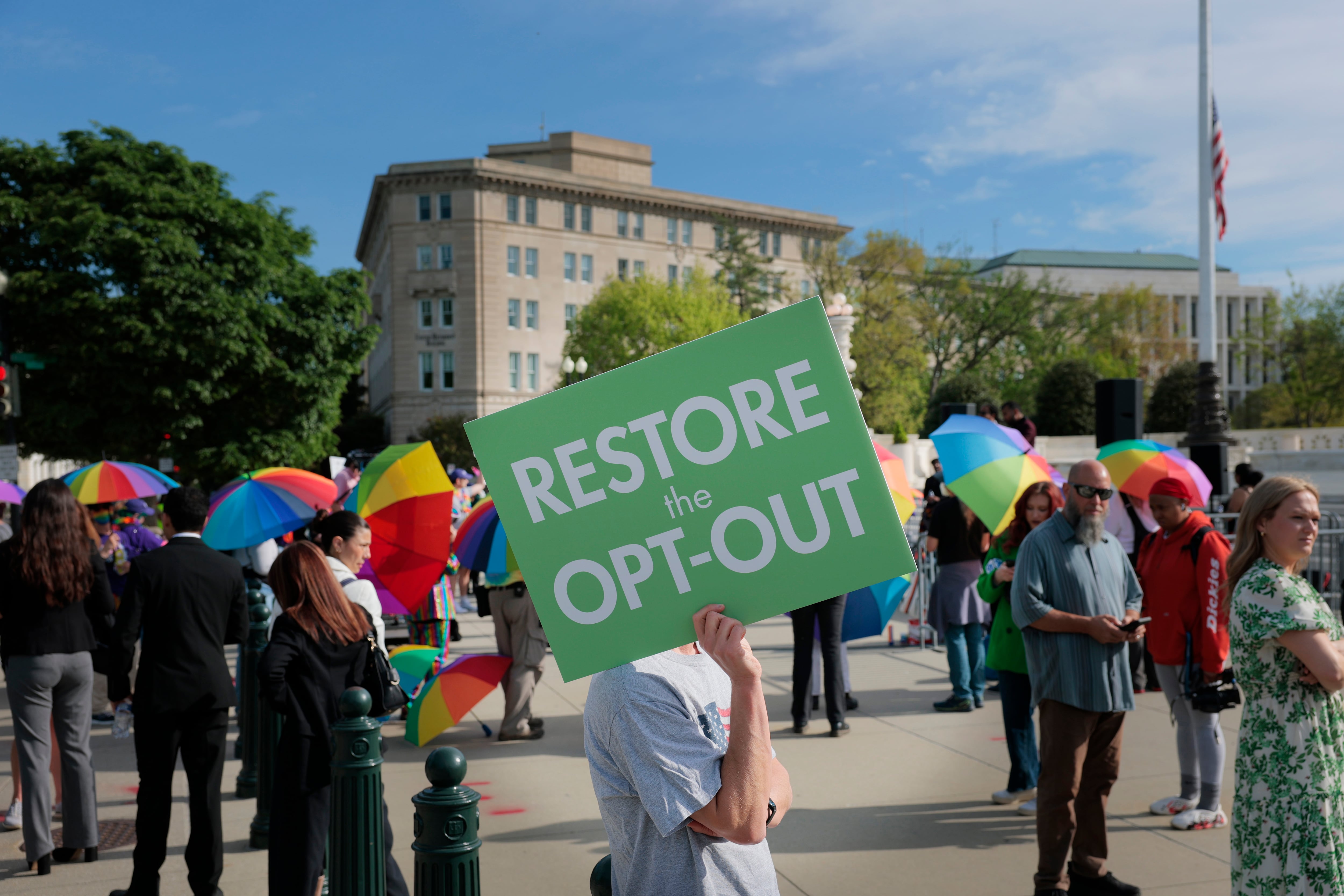 A woman holds a green sign as others mill about.
