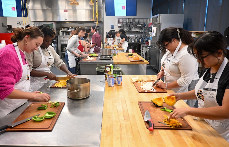 Four female students in aprons do food prep on cutting boards