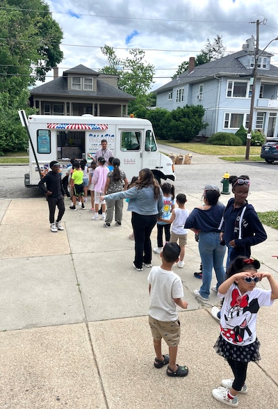 Young children line up on the sidewalk to get treats from an ice cream truck.