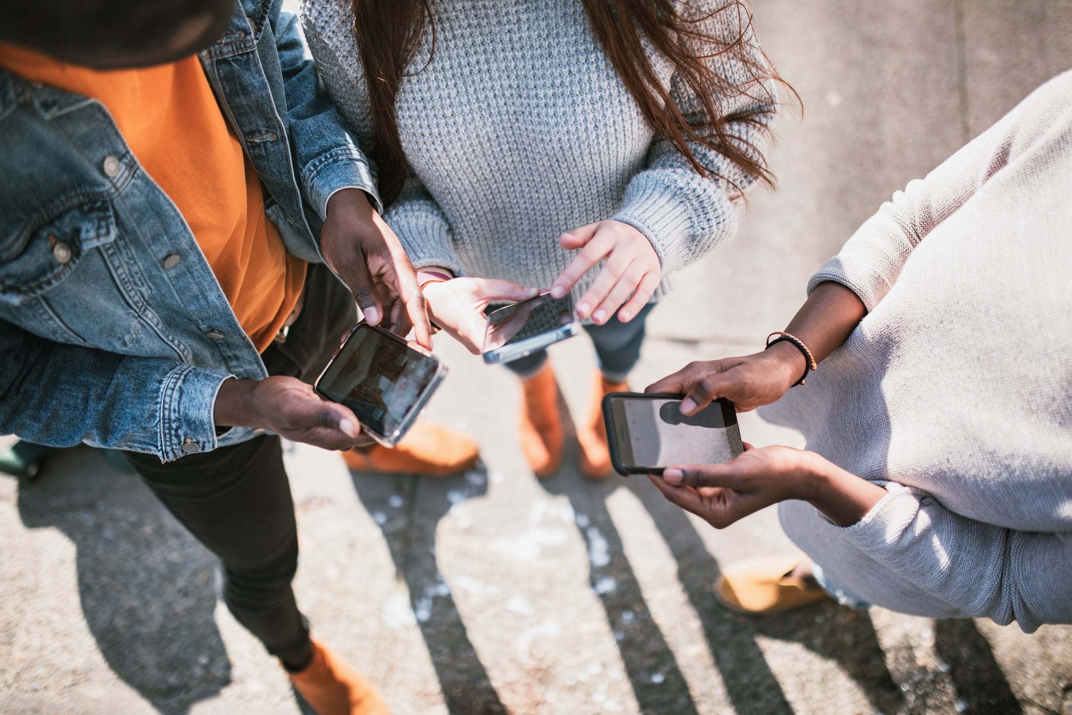 Three people in casual clothing are holding smart phones.