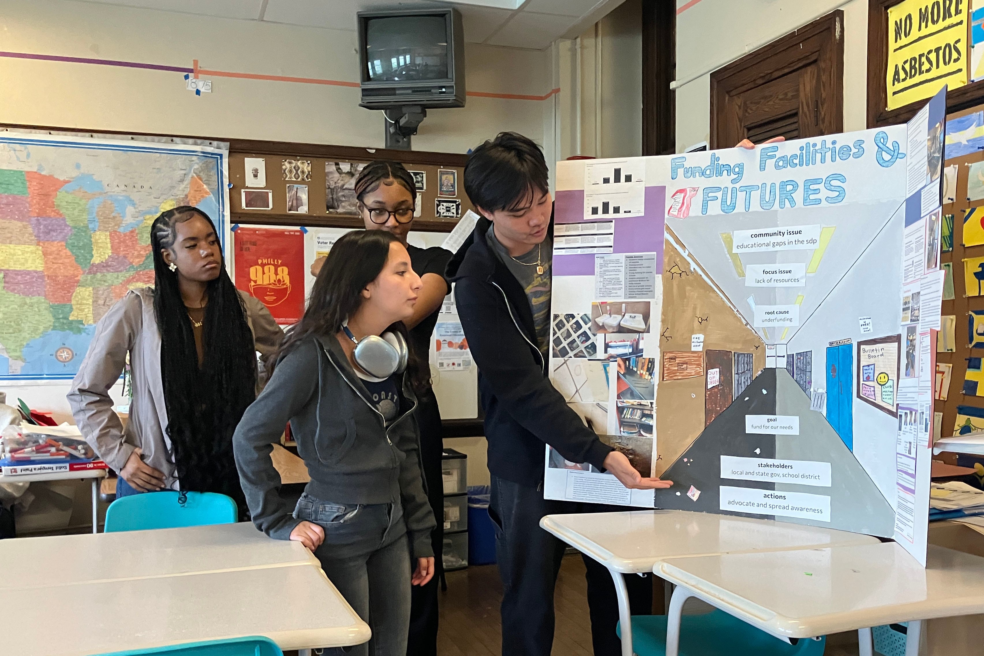 Four high school students stand next to a poster board presentation in a classroom.