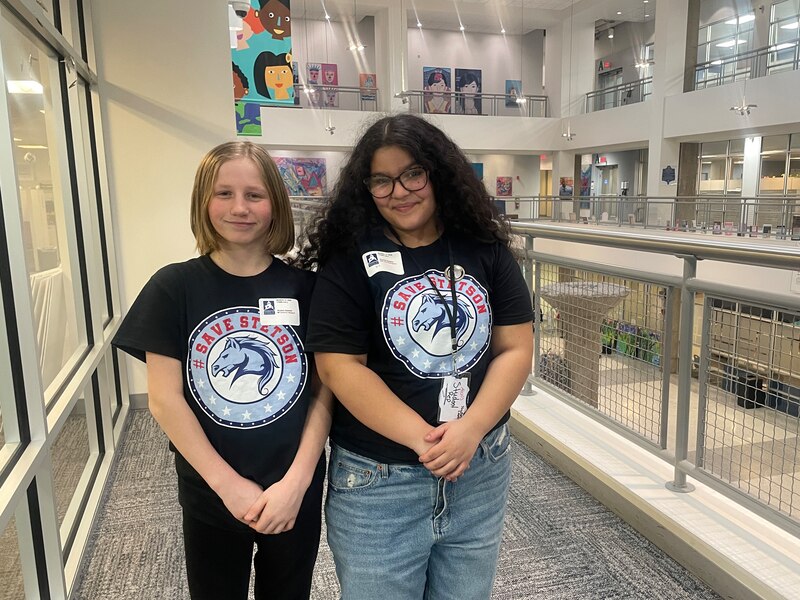 A photograph of two middle school students posing for a photograph in a hallway.